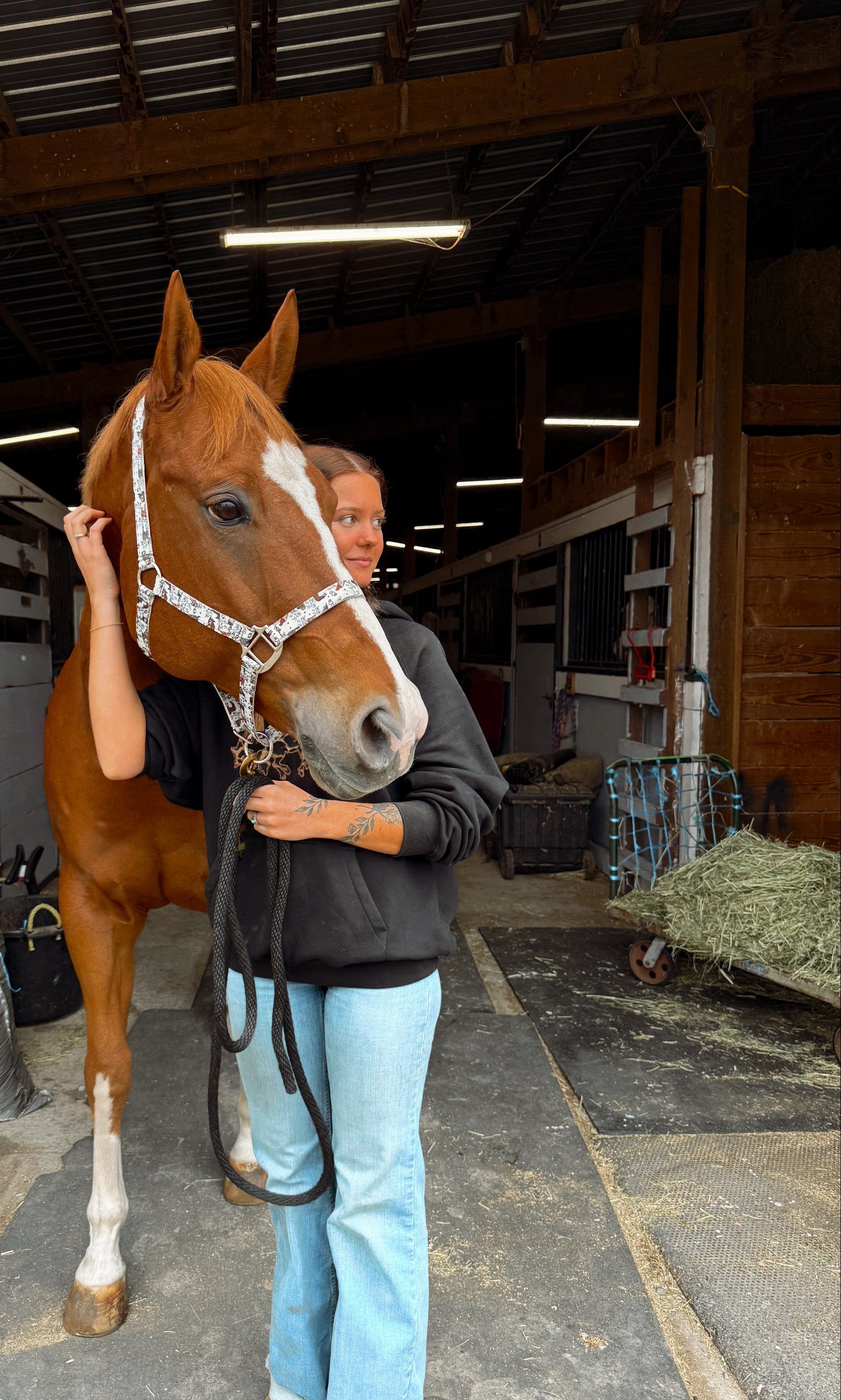 girl standing next to a brown horse in a stable wearing a leopard print hoodie