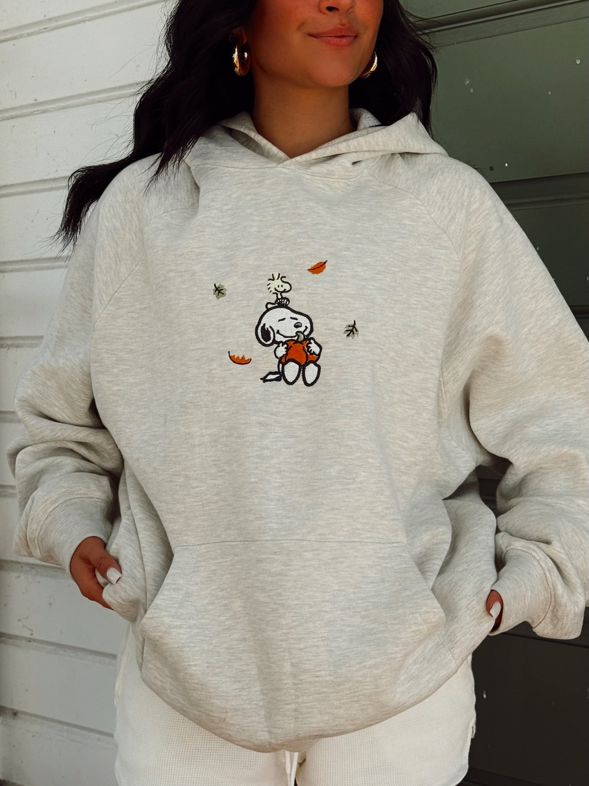 Girl wearing an oversized embroidered hoodie with a fall snoopy design in grey